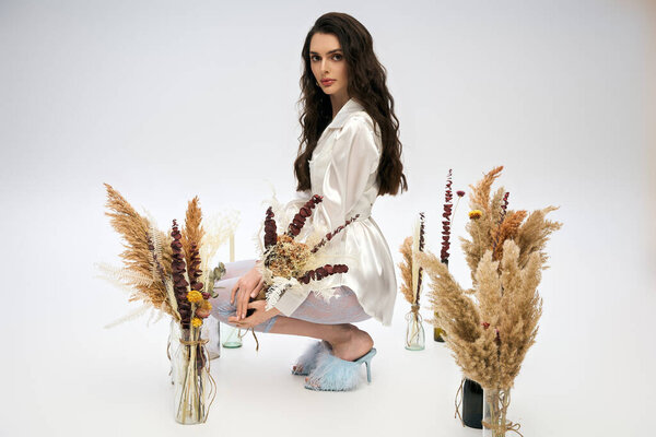 A beautiful young woman with brown hair gracefully poses among colorful flowers, radiating joy.