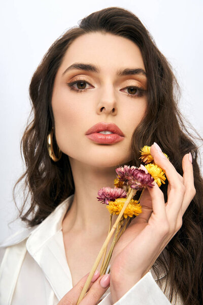 Молодая женщина с каштановыми волосами мягко держит яркие цветы, излучающие весеннюю красоту.