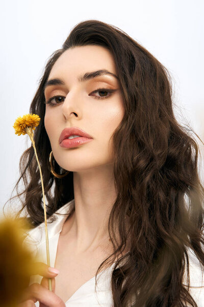 Красивая молодая женщина с каштановыми волосами держит желтый цветущий цветок
