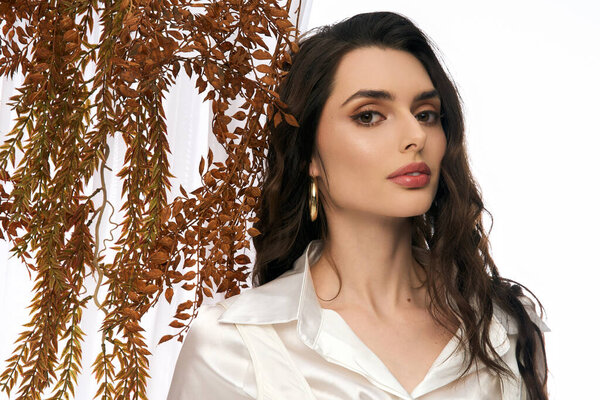 Потрясающая молодая женщина с каштановыми волосами наслаждается моментом среди ярких листьев этой весной.