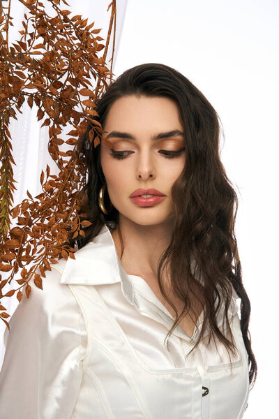 Красивая молодая женщина с каштановыми волосами взаимодействует с яркими листьями в весенней обстановке.