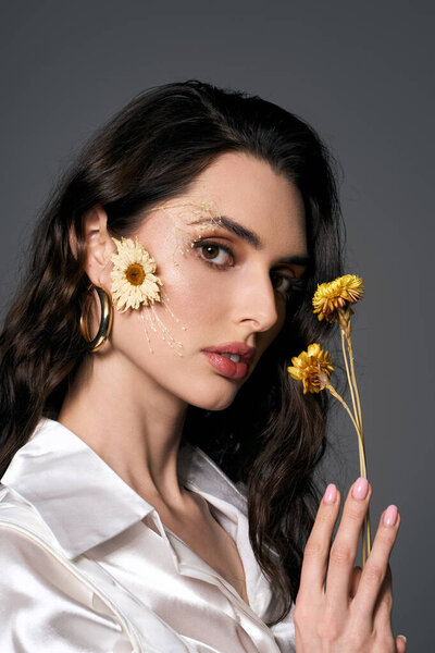 Красивая молодая женщина с каштановыми волосами держит цветы, демонстрируя спокойную и художественную весеннюю атмосферу.