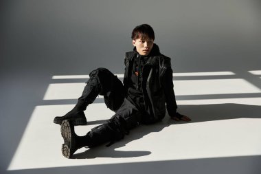 Yakışıklı Asyalı adam zarif bir şekilde yerde oturuyor ve şık kıyafetini parlak bir odada sergiliyor.