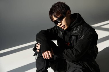 Yakışıklı, siyah giyinmiş genç adam hafif aksanlara karşı kendine güvenen bir poz veriyor..