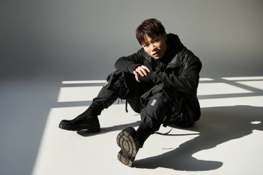 Şık bir Asyalı genç adam, kentli moda eğilimlerini sergileyerek, kendinden emin bir şekilde yerde oturuyor..