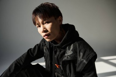 Siyah giyinmiş yakışıklı genç adam minimalist bir ortamda düşünceli bir şekilde poz veriyor..