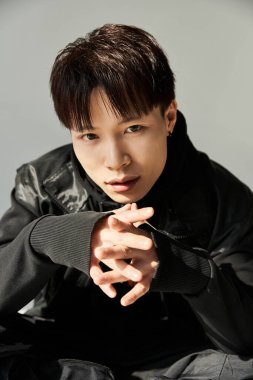 Şık Asyalı genç adam kendinden emin oturuyor, büyüleyici bir ifadeyle modern bir görünüm sergiliyor.