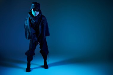 Genç, şık Asyalı bir adam büyüleyici mavi bir atmosferde modern moda seçimleri sergiliyor..