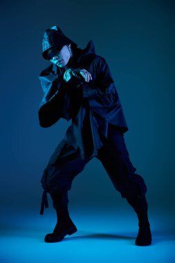 Yakışıklı Asyalı adam canlı mavi ışık altında göz alıcı kıyafetiyle dinamik bir poz veriyor..