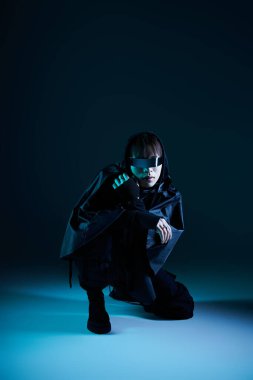 Şık bir Asyalı kendine güvenerek çömelmiş modern moda eğilimlerini sergiliyor..