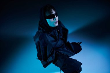 Genç, yakışıklı Asyalı bir adam, koyu mavi ışıklarla aydınlatılan modern bir elbiseyle güvenle ayakta duruyor..