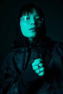 Yakışıklı genç adam, karanlık bir arkaplanda kendine güvenen bir poz verirken modern bir görünüm sergiliyor..