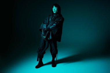 Yakışıklı Asyalı bir adam, parlak mavi ışıkla aydınlatılmış, gösterişli bir kıyafetin içinde zahmetsizce duruyor..