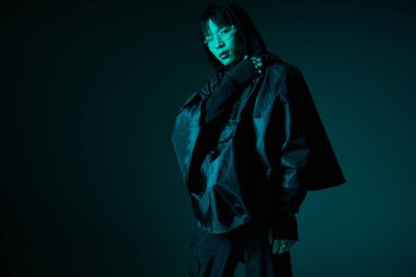 Kendine güvenen Asyalı genç adam düşük ışıkta şık siyah kıyafetler sergiliyor..