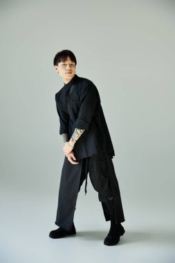 Yakışıklı genç adam basit bir arkaplana karşı şık siyah kıyafetler içinde güven içinde poz veriyor..