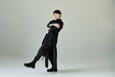 Genç, yakışıklı Asyalı bir adam şık bir siyah elbise içinde duruyor ve poz veriyor..