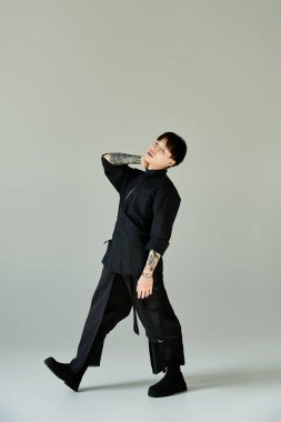 Dövmeli bir genç adam basit bir ortamda şık bir poz verir..