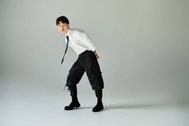 Modaya uygun genç bir adam, kapalı mekanda benzersiz bir duruşta dururken modern stili özel bir şekilde sergiliyor..