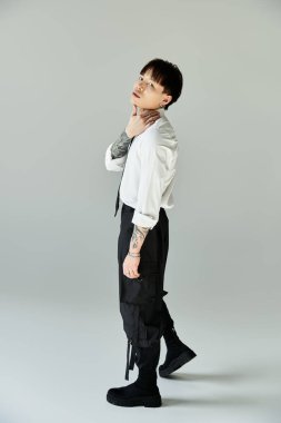 Dövmeli bir genç adam kendine güvenerek şık bir şekilde poz verir, yumuşak ışık altında cazibe yayar..