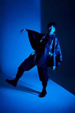 Şık bir Asyalı genç adam çarpıcı mavi ışıkların altında modern bir kıyafetle poz veriyor..