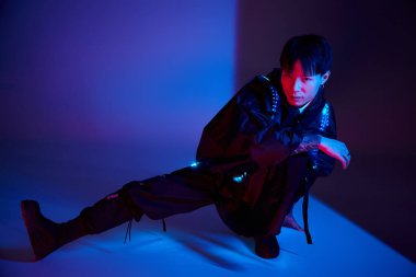 Yakışıklı Asyalı genç adam renkli bir ışığın ortasında dikkat çekici bir kıyafetle rahatça poz veriyor..