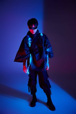 Havalı, mavi ve mor ışıklara karşı poz veren Asyalı şık bir adam modern modayı sergiliyor..