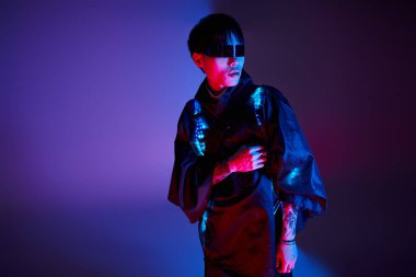 Genç Asyalı adam renkli ışıklar altında geleneksel ve modern tarzın bir karışımını sergiliyor.