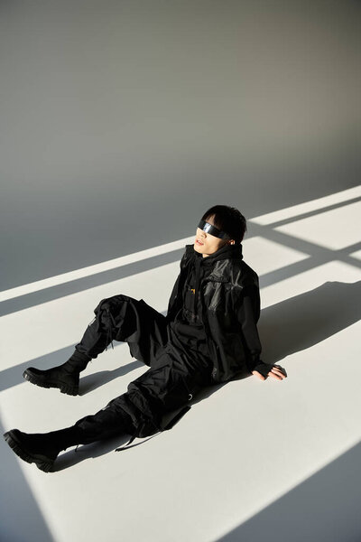A young Asian man in all black lounges on the floor amidst striking light patterns.