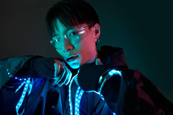 Красивый молодой человек демонстрирует свой яркий стиль с освещенными элементами в темной среде.