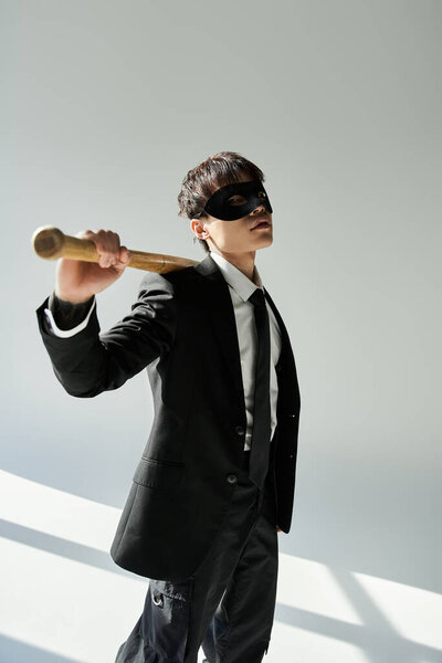 Красивый молодой азиат, одетый в официальный костюм, уверенно держит летучую мышь в маске..