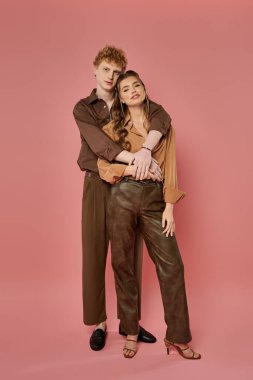 İki genç aşık, canlı bir ortamda neşeyle kucaklaşırken modern giysiler sergiliyor.