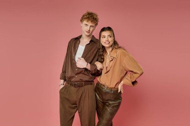 Pembe bir arka planda iki şık kişi neşe içinde poz veriyor..