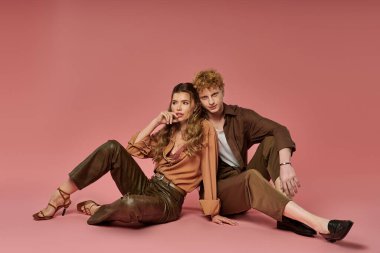 Moda kıyafetleri içinde genç bir çift, yumuşak pembe bir arka plana karşı aşk yayıyor..