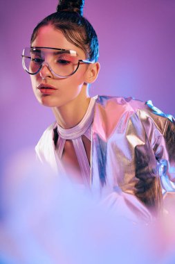 Metalik kıyafetli genç bir kadın holografik renklerin ortasında parıldıyor, modern tarz yayıyor..