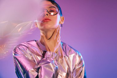 Şık bir kadın holografik renklere ve çarpıcı modern aksesuarlara sahip fütüristik giysiler sergiliyor..