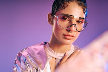 Metalik giyimli genç bir kadın canlı bir arka plana karşı, kendinden emin bir şekilde duruyor, çağdaşlık saçıyor..