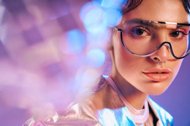 Genç bir kadın renkli bir sahnede canlı bir holografik kıyafet ve şık aksesuarlar içinde göz kamaştırıyor..