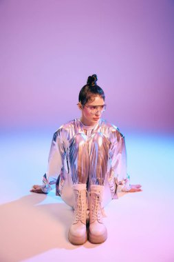 Holografik giyinmiş genç bir kadın zarif bir şekilde oturur, stil ve güven yayar..