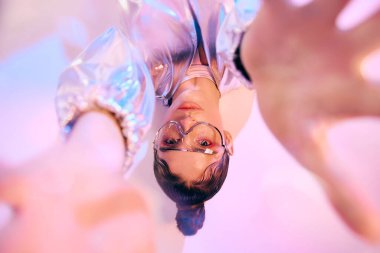 Genç bir kadın modern holografik kıyafetini renkli ve deneysel bir sahnede modelliyor..