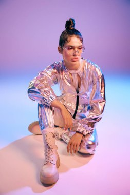 Holografik kıyafetli genç bir kadın şık bir şekilde poz verir, canlı bir ortama güvenir..