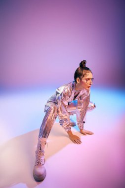 Genç bir kadın deneysel bir holografik kıyafet içinde modern moda titreşimleri yayarak zarifçe poz veriyor..