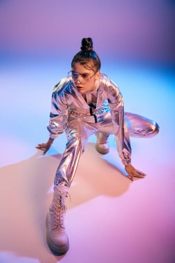 Şık bir kadın renkli bir arkaplana karşı canlı holografik giysiler içinde poz verir..