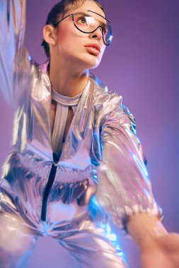 Metalik giyinmiş genç bir kadın, kendine güvenerek renkli bir arkaplanda poz veriyor..