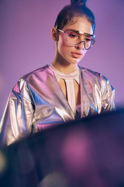 Genç bir kadın renkli bir arkaplana karşı canlı bir holografik kıyafet modelliyor..