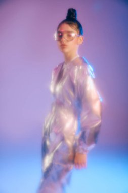 Genç bir kadın şık holografik kıyafetini canlı ve enerjik bir mekanda sergiliyor..