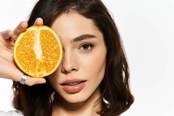 A joyful young woman playfully poses with a bright orange slice by her face.