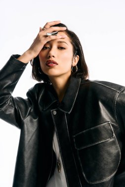 Kendine güvenen genç bir kadın zarif pozlar veriyor, şık tarzını deri ceketiyle ön plana çıkarıyor..