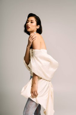 Dengeli bir gelin büyüleyici elbisesini tarafsız bir arkaplanda sergiliyor..