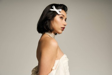 Güzel, genç bir gelin zarif bir şekilde duruyor, düğün kıyafetlerini ve narin aksesuarlarını sergiliyor..