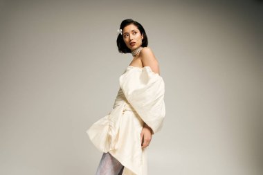 Çekici genç bir gelin zarif bir elbiseyle poz verir, güzelliğini ve duruşunu ön plana çıkarır..